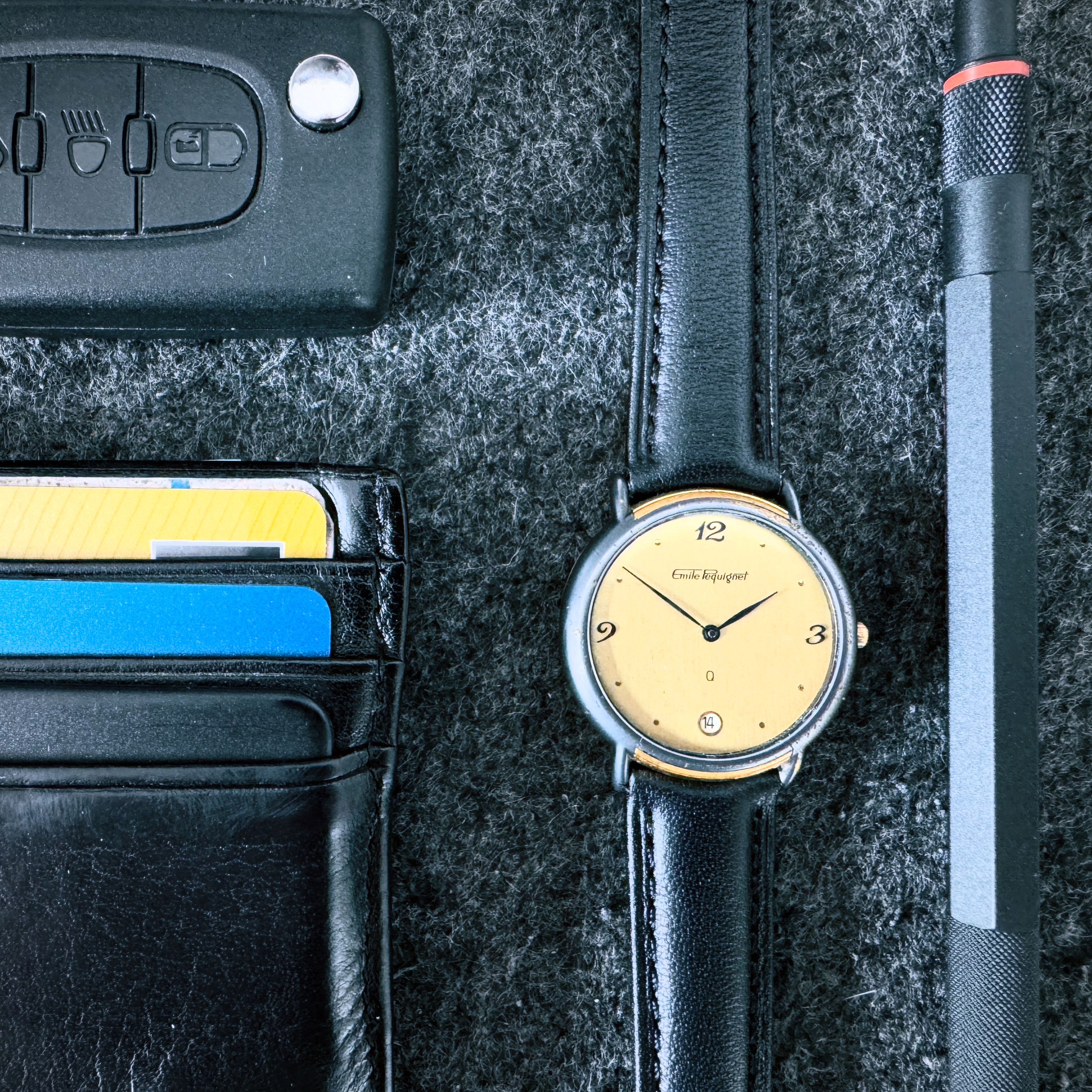 Restored Emile Pequignet watch with new black leather strap on a felt surface, alongside a wallet, car keys and watchmaker's screwdriver